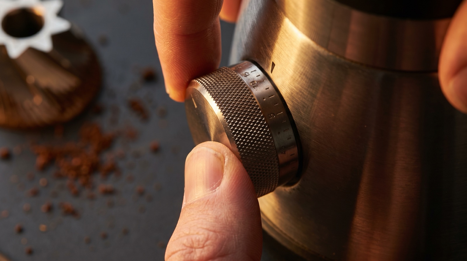 Close-up of a fingertip turning a premium espresso grinder adjustment collar, with fine grounds visible in the background.