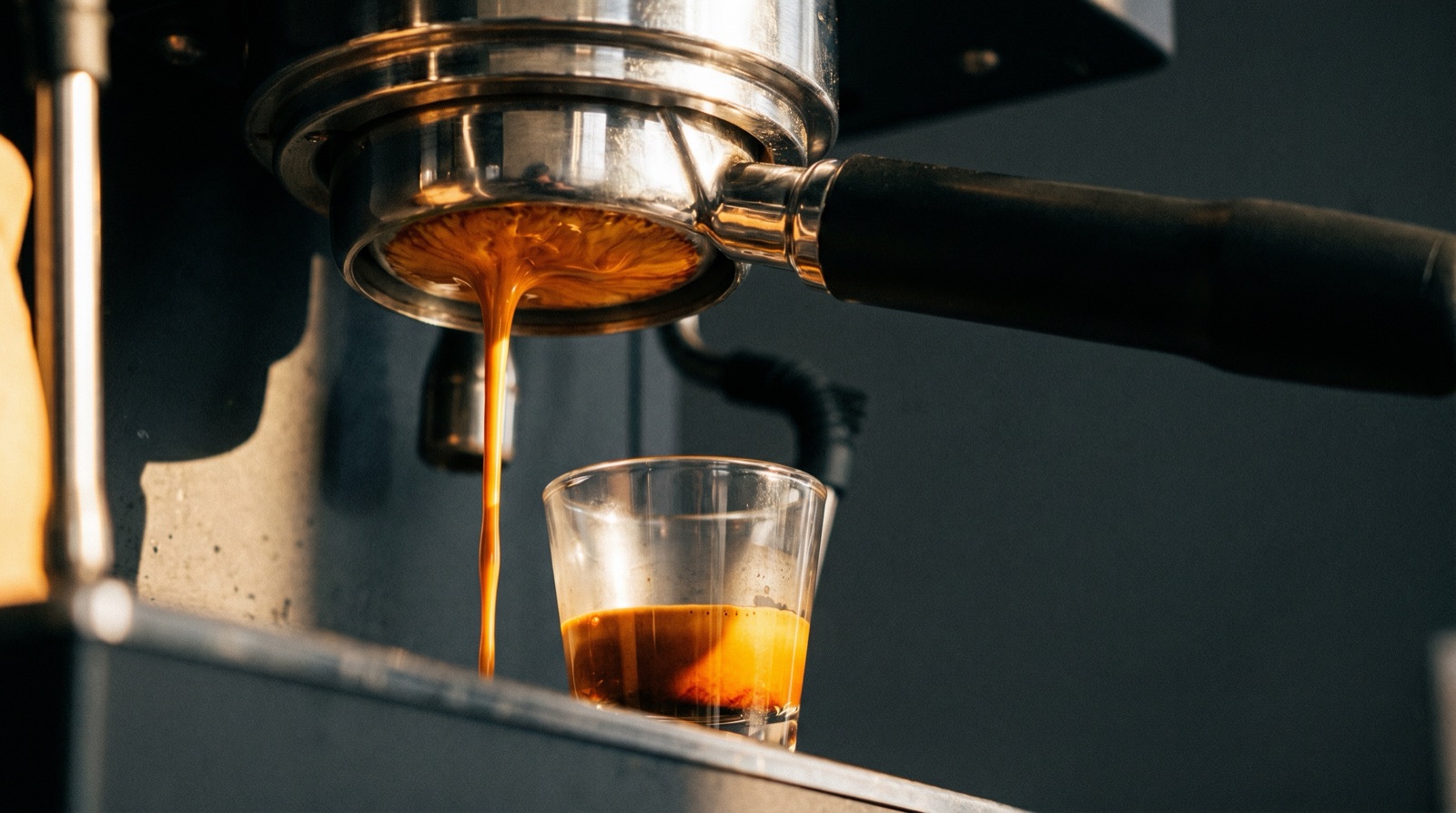 A bottomless naked portafilter showing a thick amber espresso stream flowing into a small glass cup below.